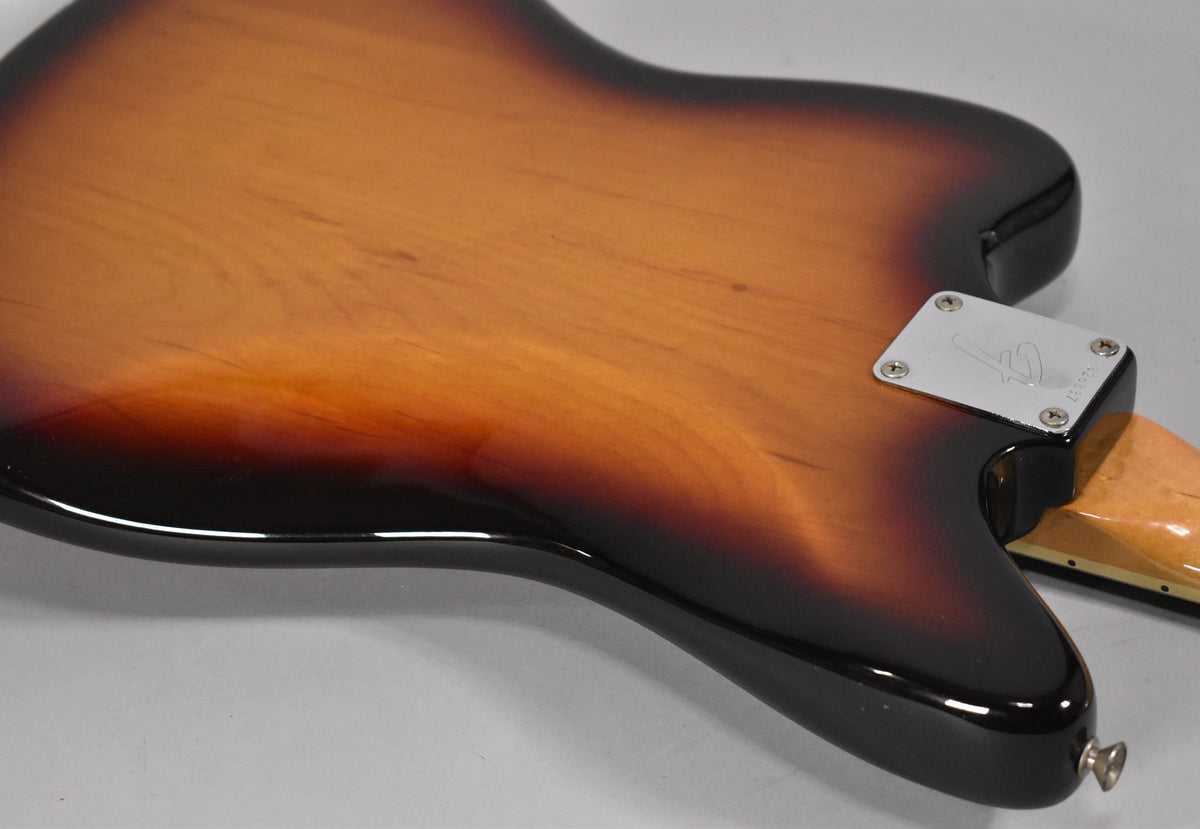 The guitar's sunburst body, viewed from the back, shows light wear and a chrome neck plate with a visible serial number.