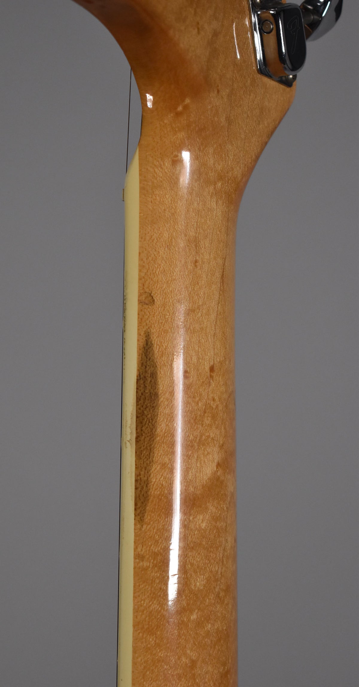 The guitar's maple neck and headstock are shown from behind, revealing a dark wear patch and finish checking on the neck.
