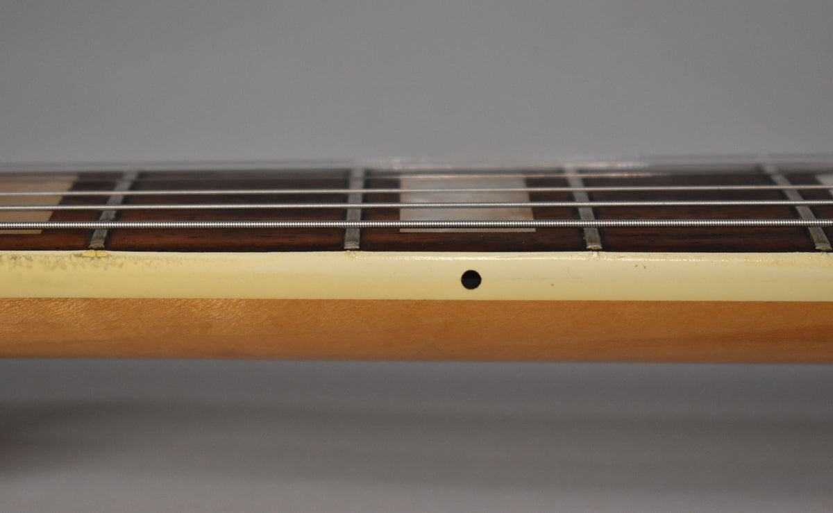 Close-up of the guitar's fretboard and neck, showing dark wood, white binding with a black side dot, and visible wear near the frets.