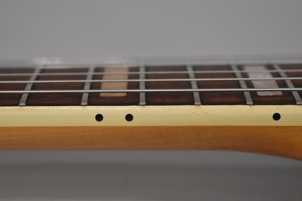 Close-up of the guitar's maple neck and dark rosewood fretboard with block inlays, showing light wear and three black side dots.