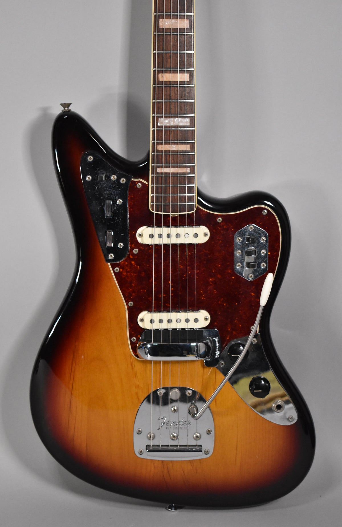 Close-up of a 3-tone sunburst electric guitar, showing the body, dark tortoiseshell pickguard, two white pickups, and chrome hardware.