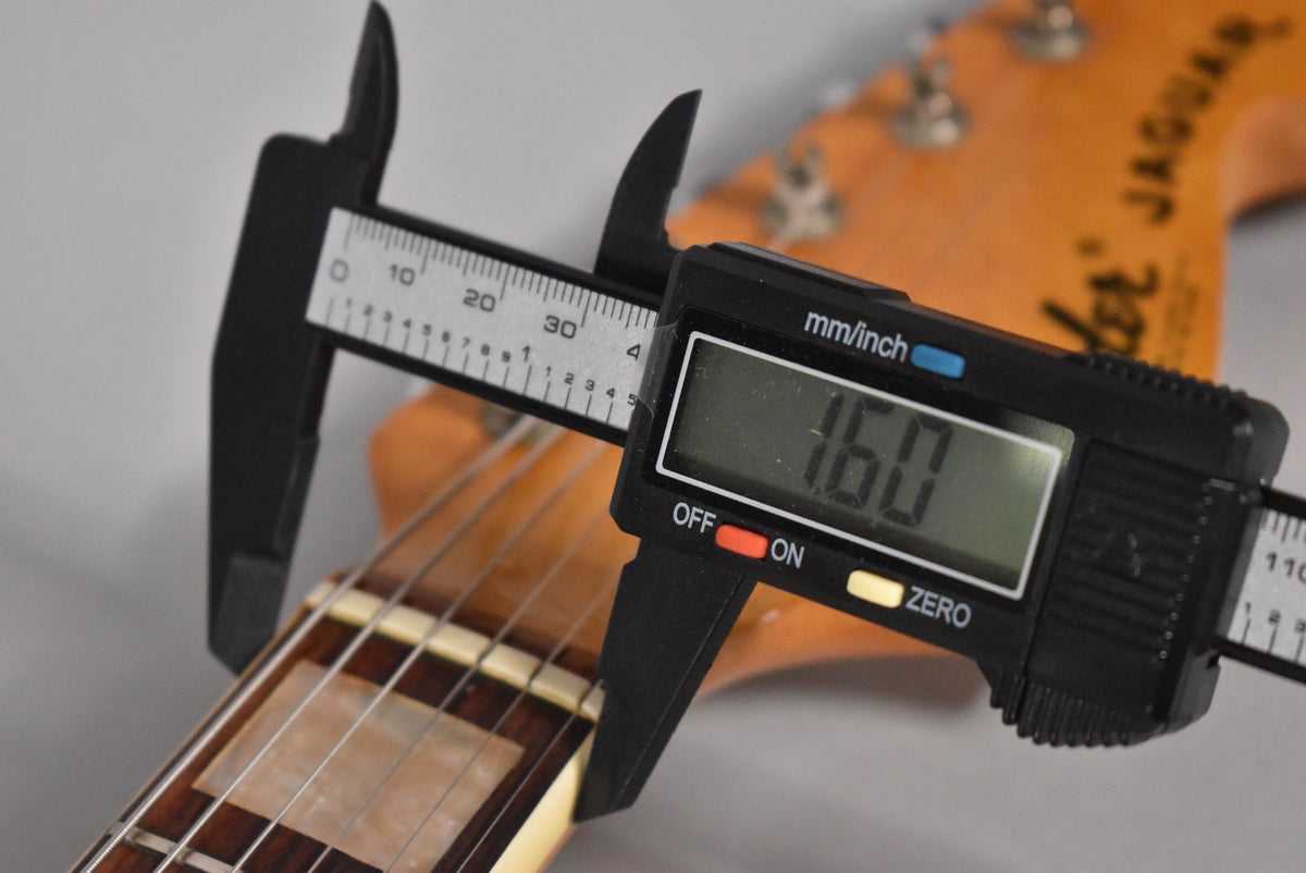 Digital calipers measure the nut width of the dark rosewood fretboard to 1.60 inches, with block inlays visible.