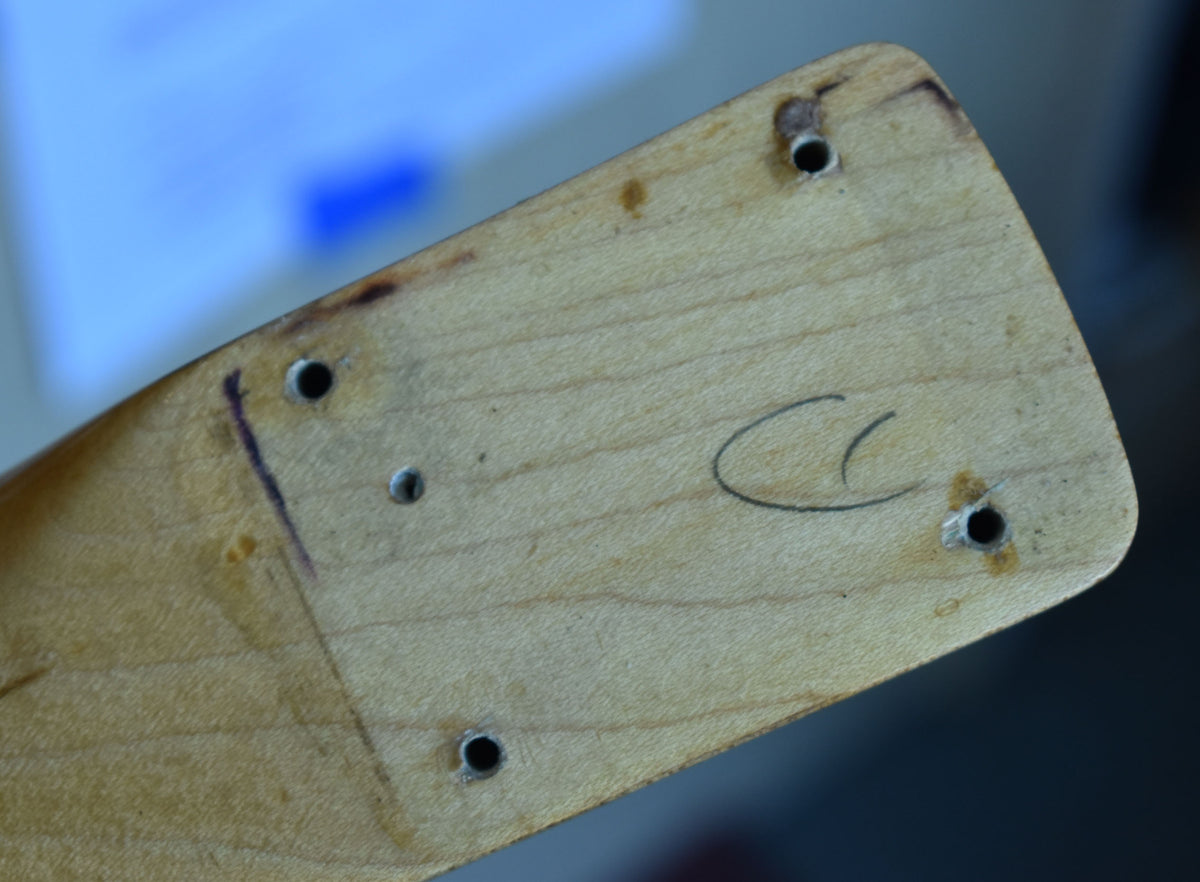 Close-up of the guitar neck heel, showing four screw holes, a faint pencil mark, and a handwritten "CC" in black ink.