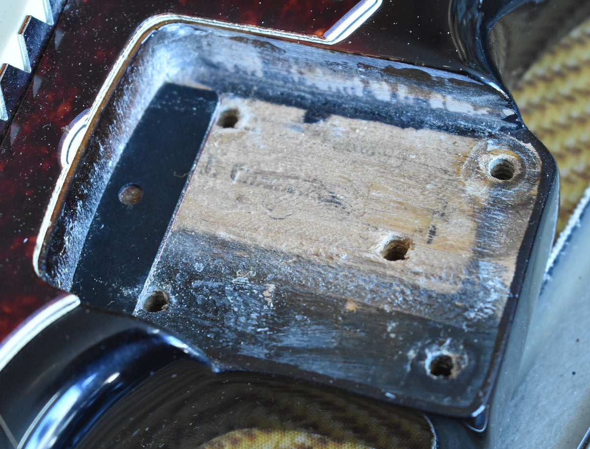 Close-up of the guitar's neck pocket, showing exposed wood, four screw holes, and some finish wear around the edges.