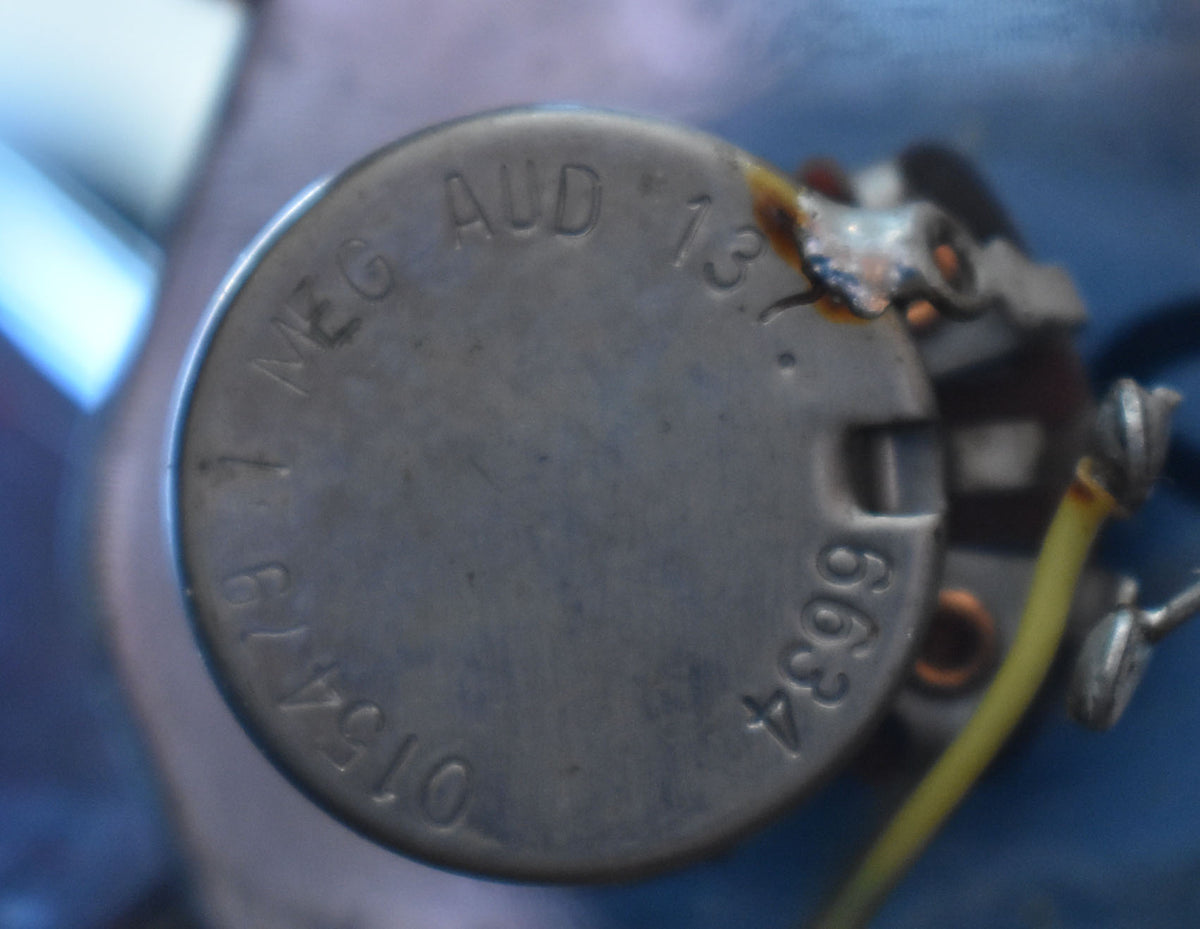 Close-up of a silver potentiometer with stamped numbers and letters, showing solder connections and a yellow wire.