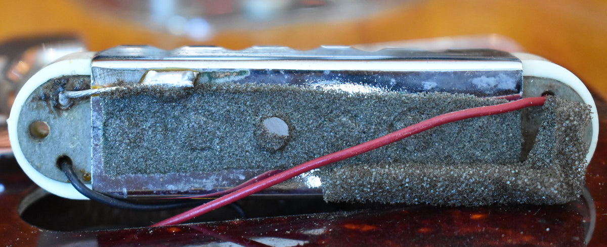 Close-up of a pickup's underside, showing the chrome cover, white bobbin, dark gray foam, and red and black wires.