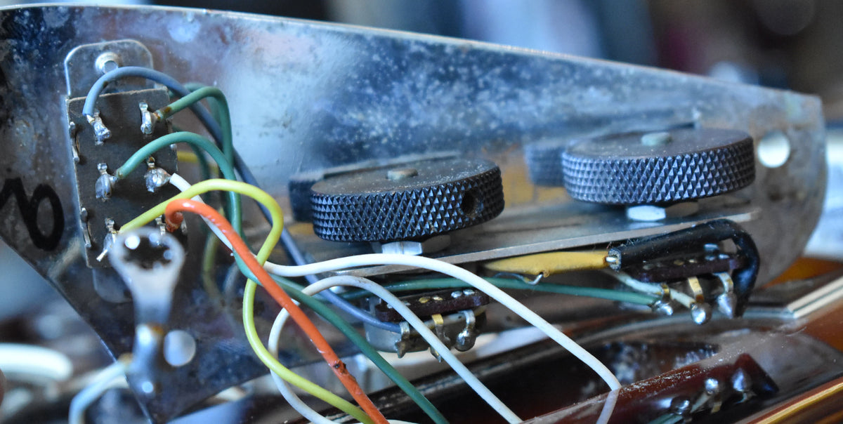 Close-up of the guitar's internal wiring, showing soldered connections, multicolored wires, and two knurled black control knobs.