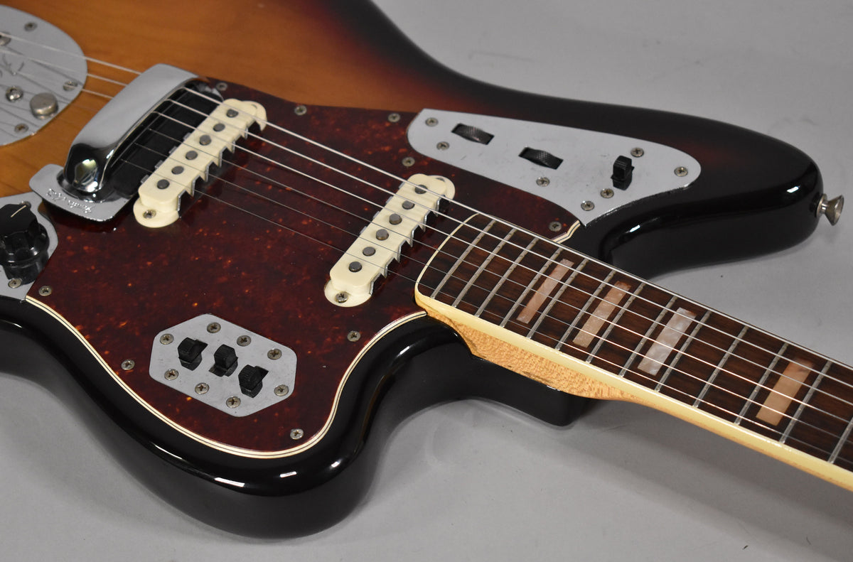 Close-up of a sunburst electric guitar, showing the tortoiseshell pickguard, white pickups, chrome bridge, and block inlays.