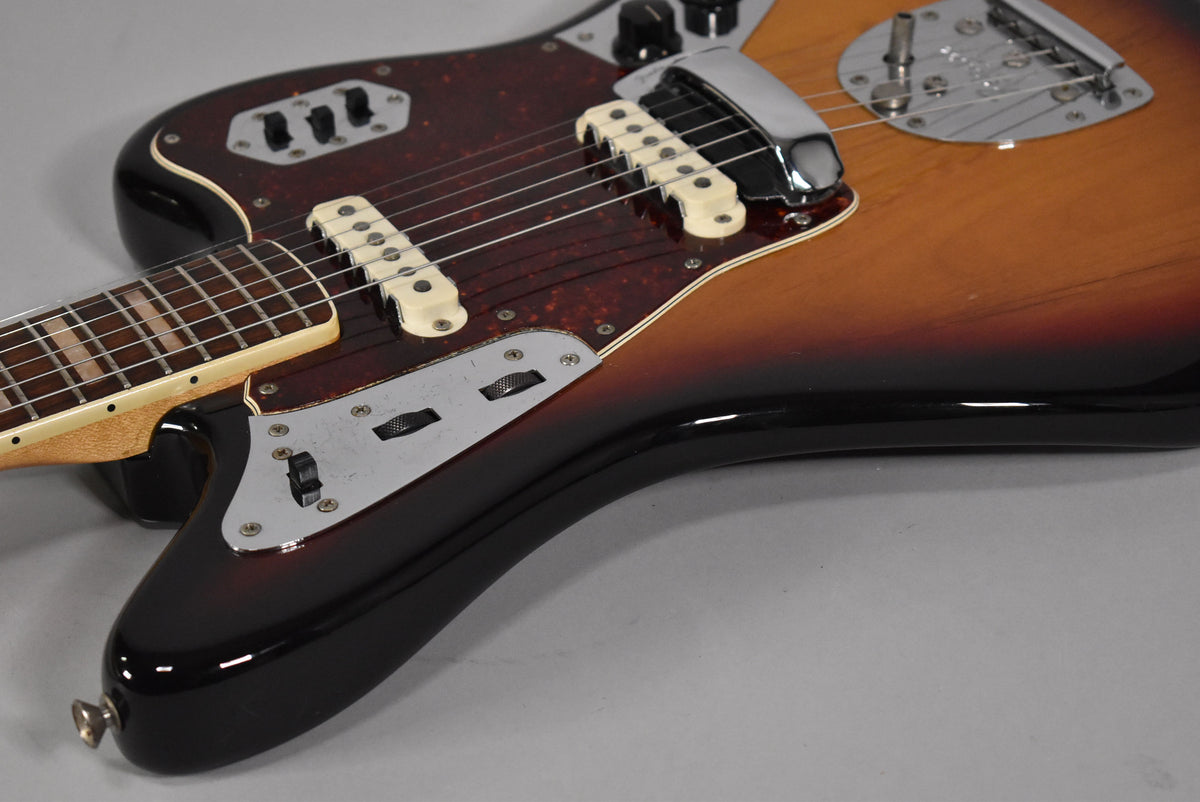 Angled view of a sunburst electric guitar, showing the body, neck, tortoise pickguard, white pickups, and chrome control plates.