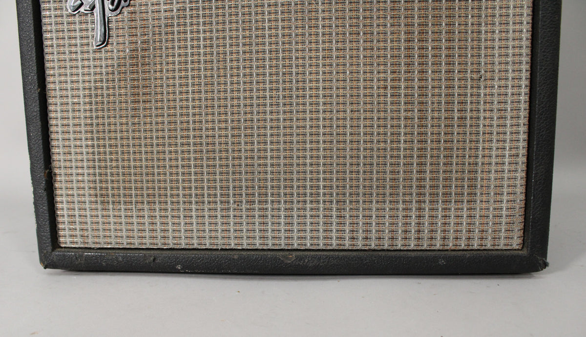 The amp's front is framed, showing the silver and tan grille cloth with a small tear, and worn black tolex on the edges.