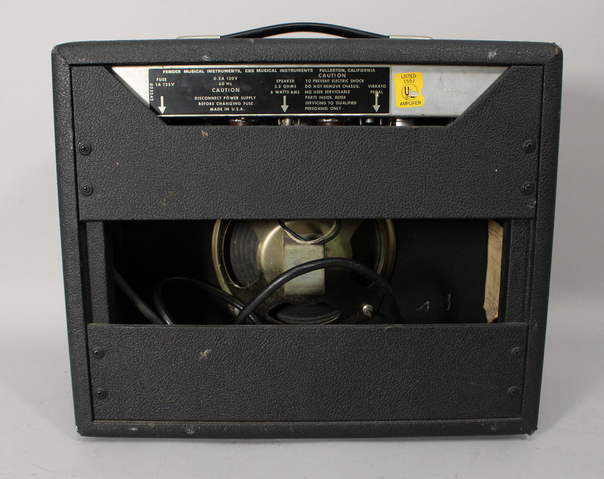 Rear view of a black textured combo amp, showing the exposed speaker, metal chassis, and various warning labels.