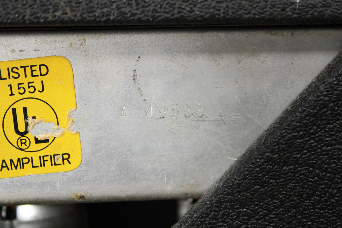 Close-up of the amp's silver metal chassis, showing a worn yellow UL sticker and faint etched numbers "A 49538".