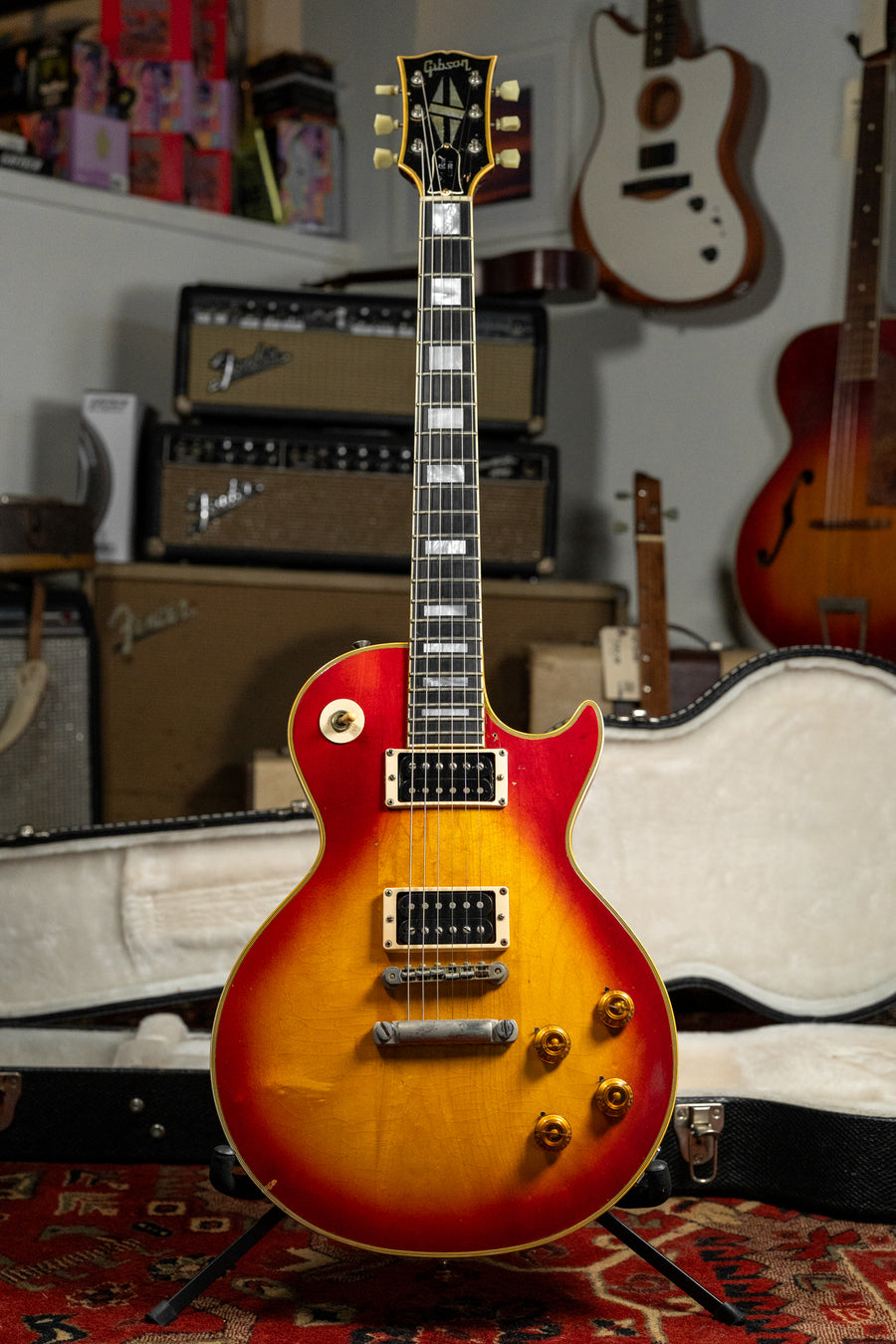 Full-length view of a cherry sunburst guitar with gold hardware and cream binding, showing light wear and checking.