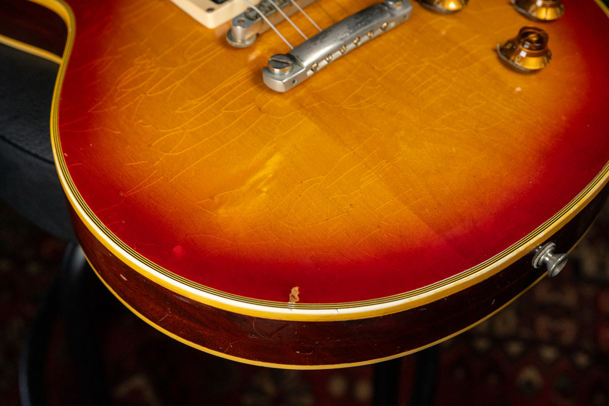 Close-up of the lower bout, showing the cherry sunburst finish with extensive checking, a chip on the binding, and a strap button.