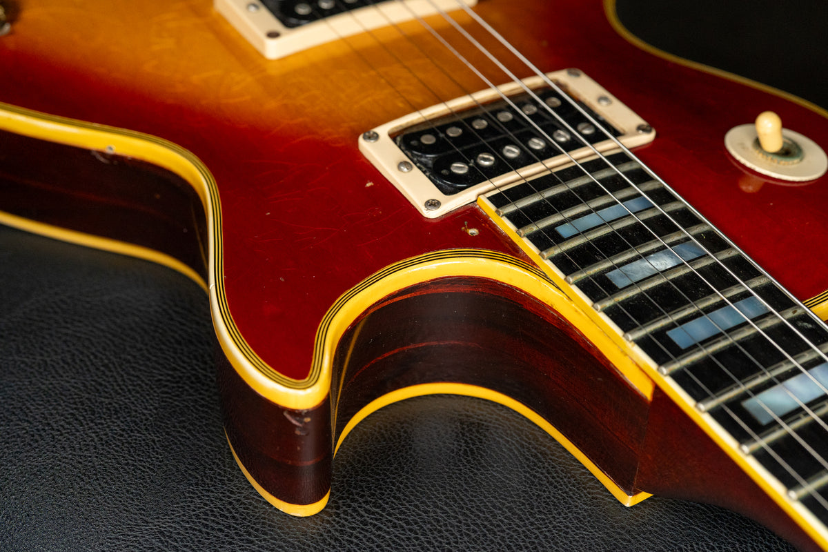 Close-up of the cherry sunburst body, showing cream humbucker pickups, trapezoid fretboard inlays, and light wear on the binding.