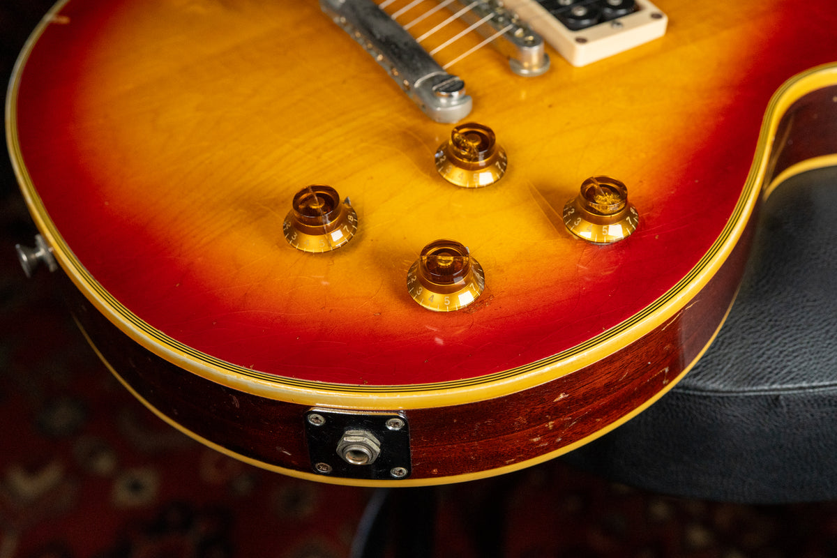 Upper body of a cherry sunburst guitar, showing four amber control knobs, output jack, and heavy finish wear on the lower bout.