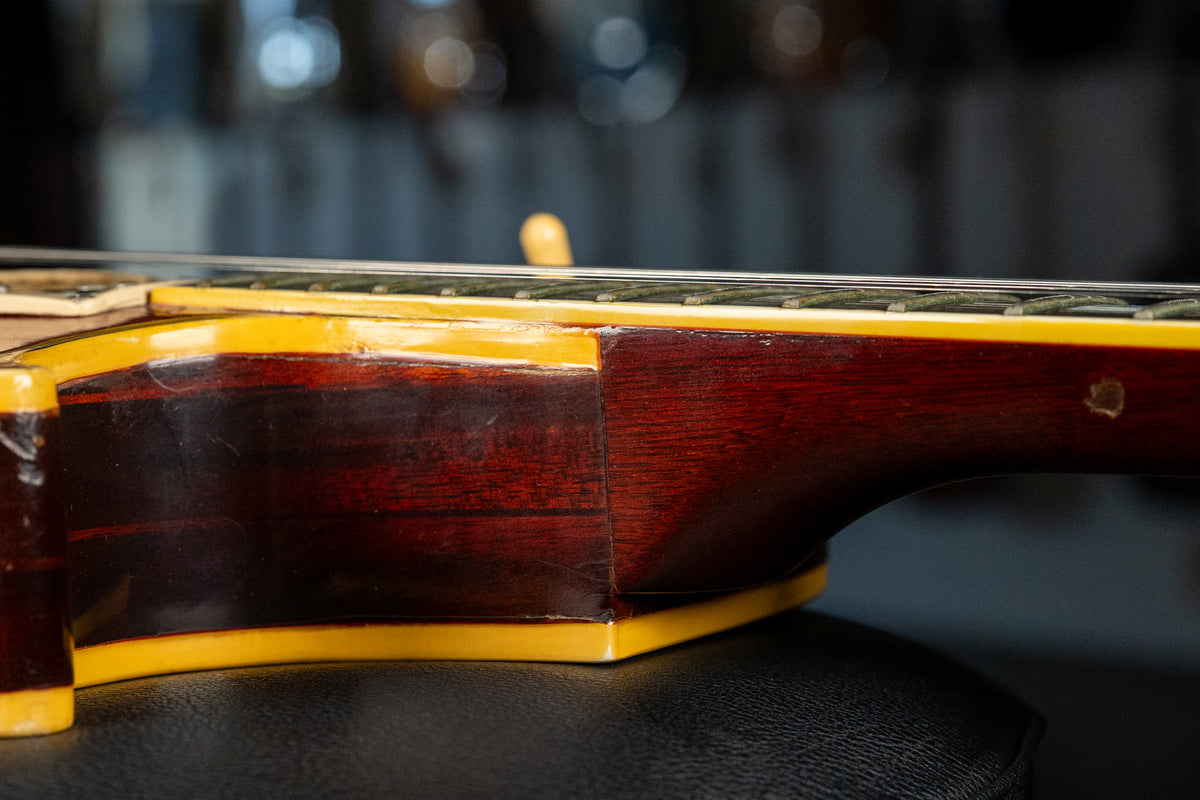 The guitar's dark cherry body and neck joint are visible from the side, with aged cream binding and light finish wear.