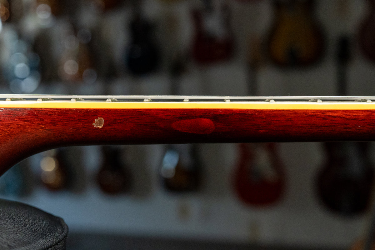 Close-up of the guitar's dark cherry neck, showing a small chip in the finish and a worn patch, with frets and binding visible.