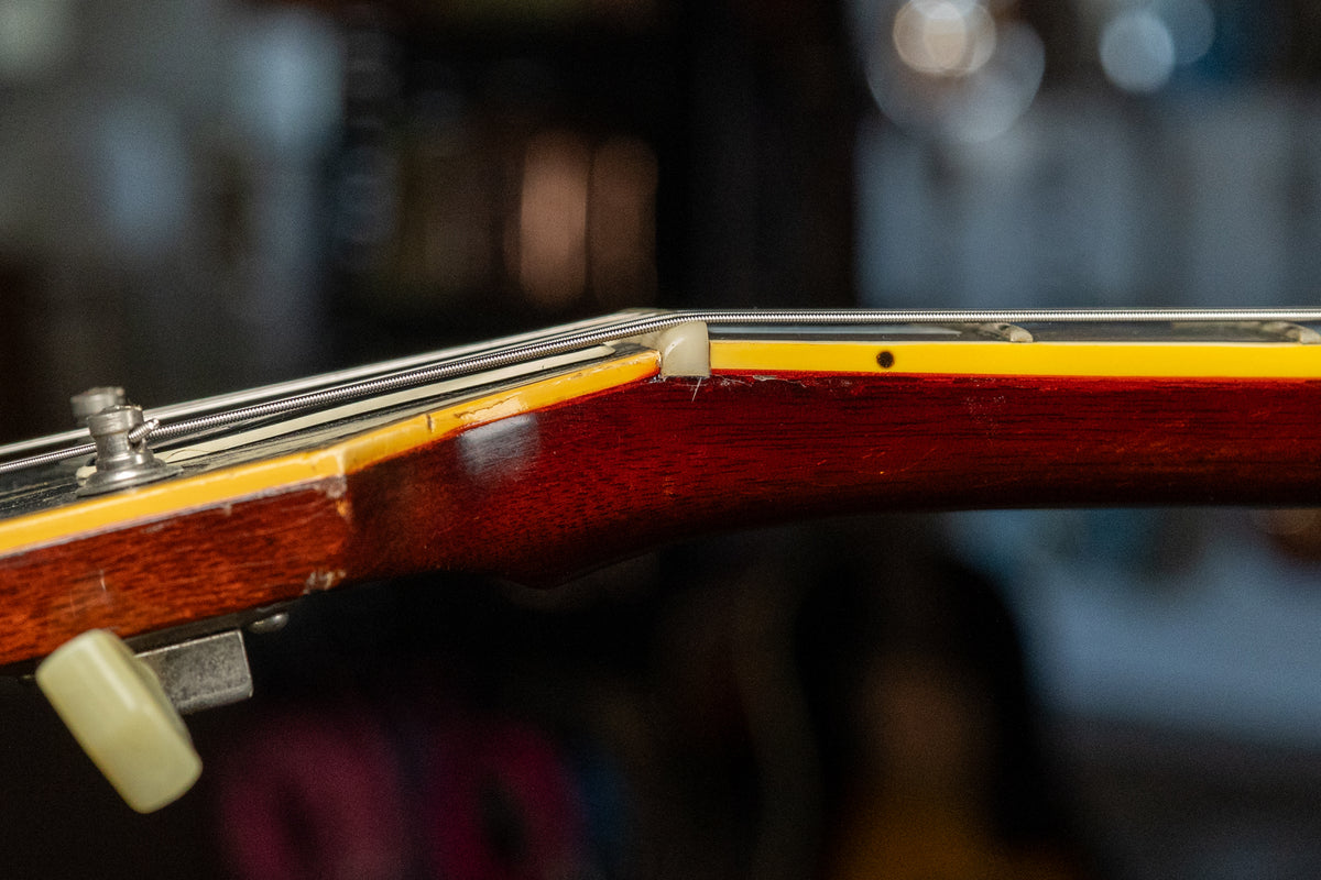 Close-up of the guitar's nut and first fret, showing the dark cherry neck, cream binding, and some finish wear near the nut.