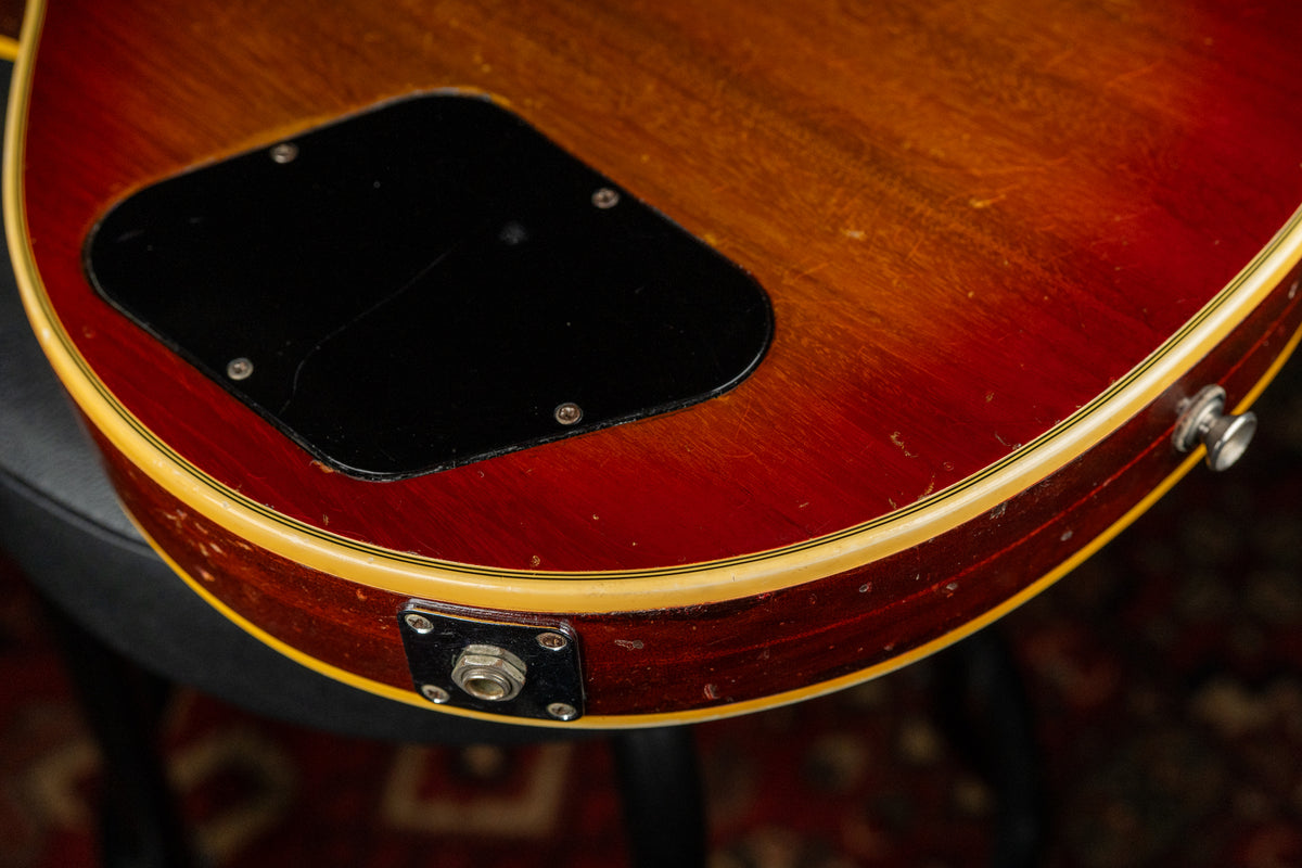 Close-up of the guitar's lower back, showing the cherry sunburst finish, black control cavity cover, output jack, and strap button, with visible wear.