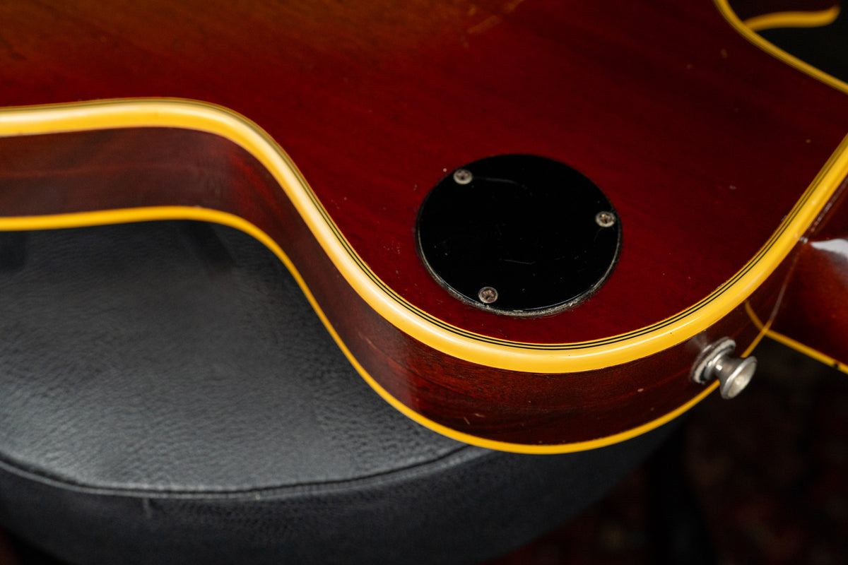 Close-up of the guitar's lower bout, showing the cherry sunburst finish, cream binding, and black control cavity cover with wear.