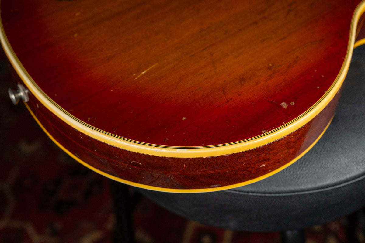 Close-up of the lower bout of a cherry sunburst guitar, showing heavy finish wear, dings, and checking along the body and binding.