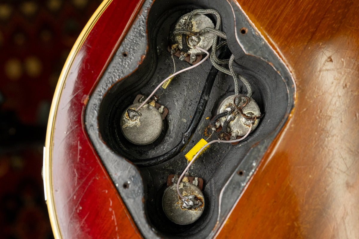 Close-up of the guitar's control cavity, revealing three worn pots, wiring, and a yellow capacitor against a dark, textured interior.