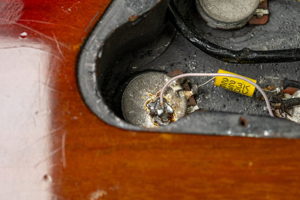 Close-up of the guitar's control cavity, revealing a potentiometer, wiring, and a yellow capacitor, with some wear on the wood.