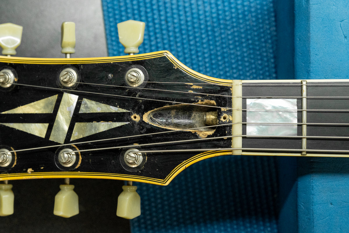 Close-up of the black headstock and fretboard, showing heavy finish wear around the exposed truss rod cavity and mother-of-pearl inlay.