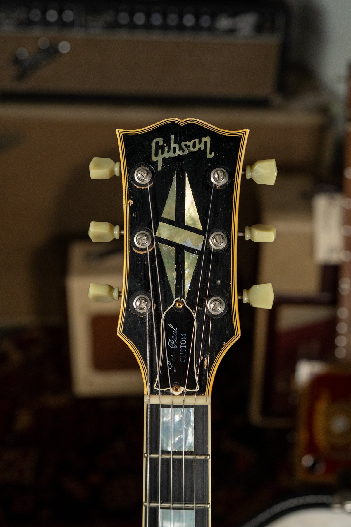 Close-up of the black headstock with cream binding, showing six aged cream tuning pegs, trapezoid inlay, and visible finish checking.
