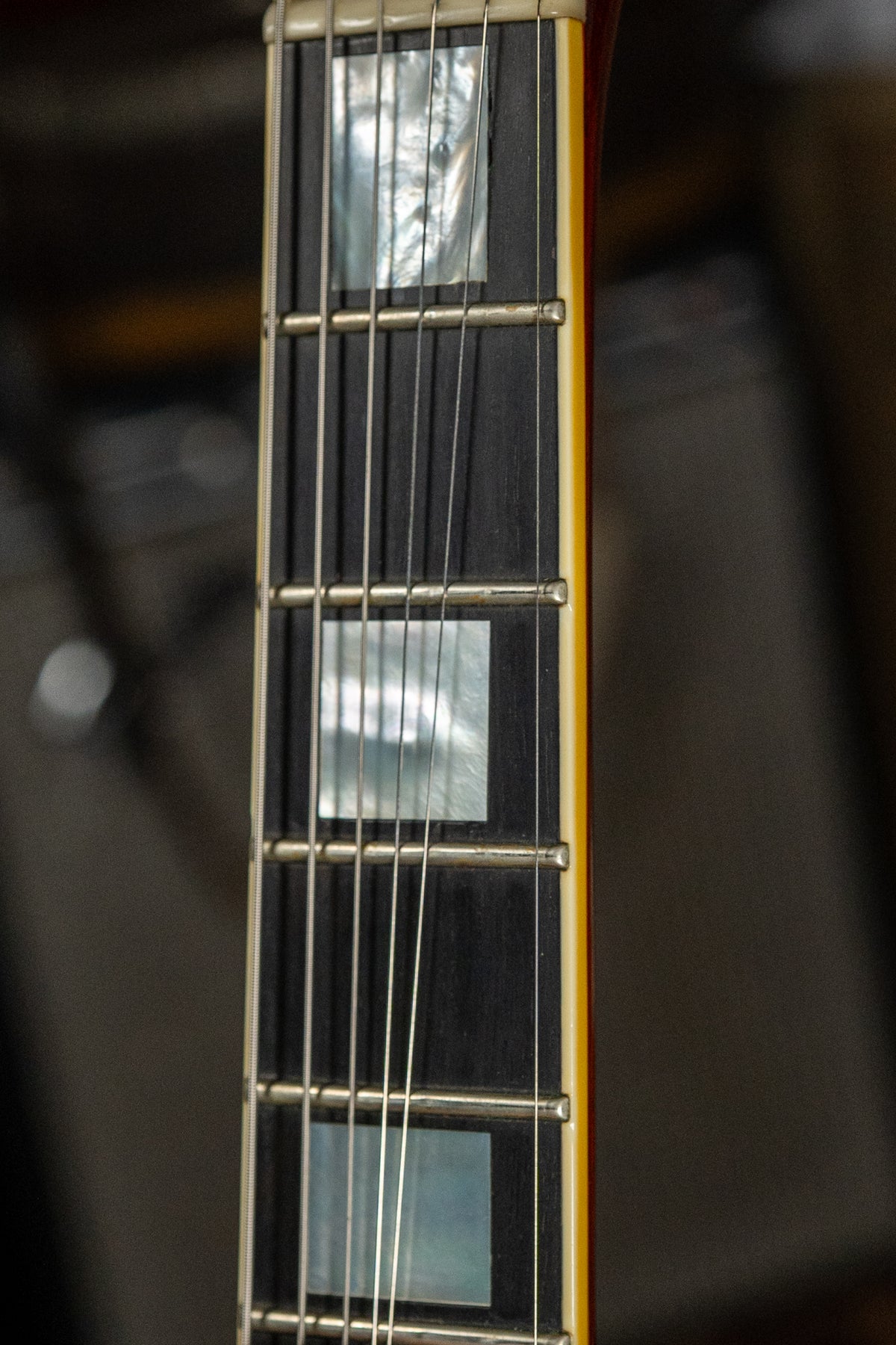 Close-up of the dark fretboard with rectangular mother-of-pearl inlays, showing light wear on the frets and cream binding.