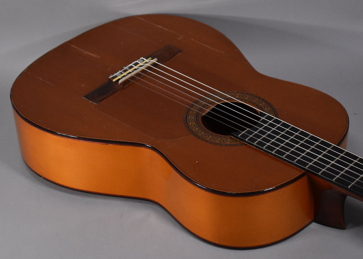 The classical guitar's natural finish top shows heavy wear and scratches, with a decorative rosette around the soundhole.