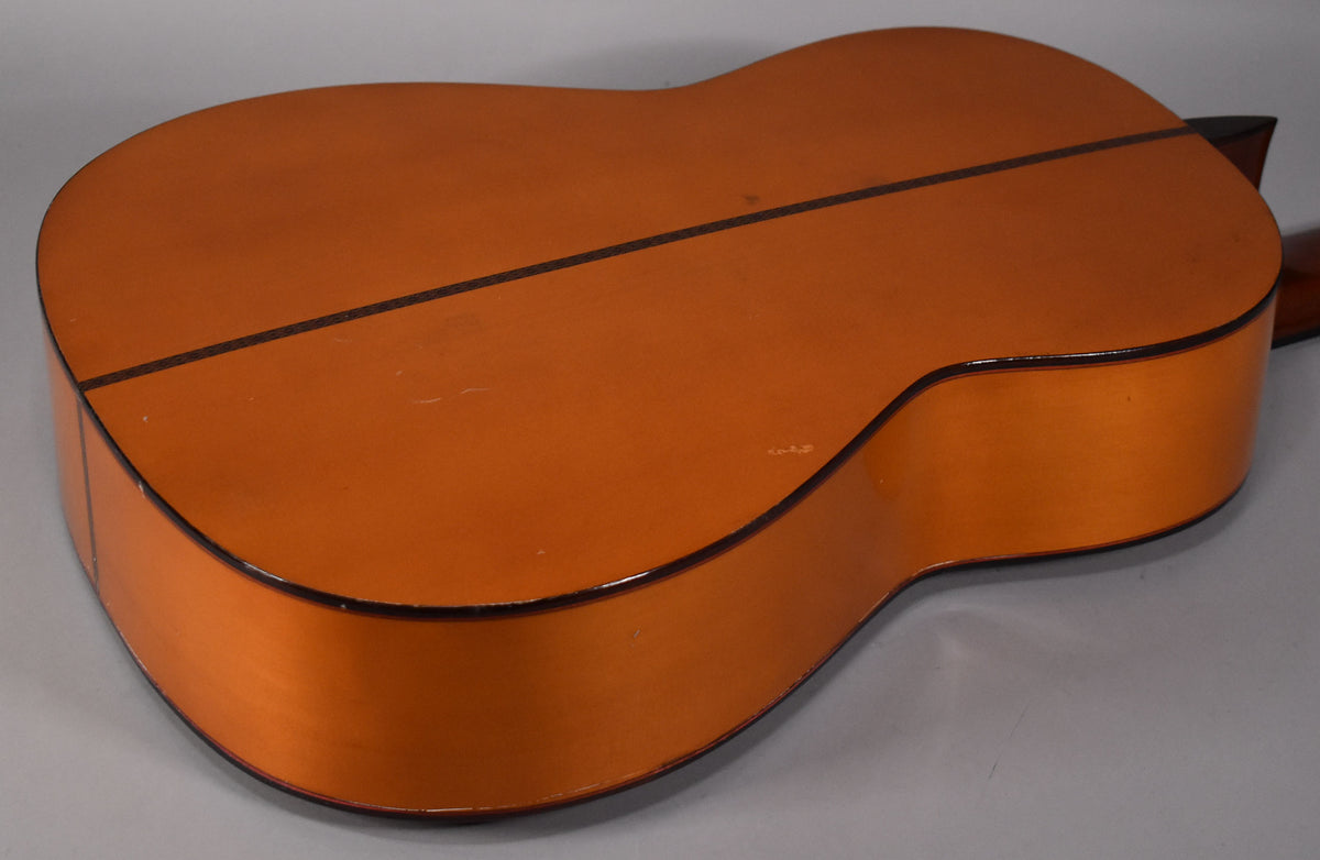 The classical guitar's natural finish back and sides are visible, with a dark center strip and binding, showing light surface wear.