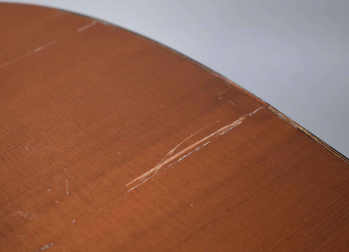 Close-up of the natural finish classical guitar's lower bout, showing deep scratches and wear on the top surface.