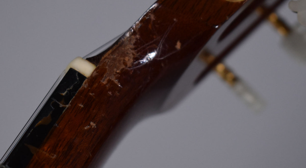 Close-up of the guitar's nut and headstock, showing significant finish wear, chipping, and checking on the dark brown wood.