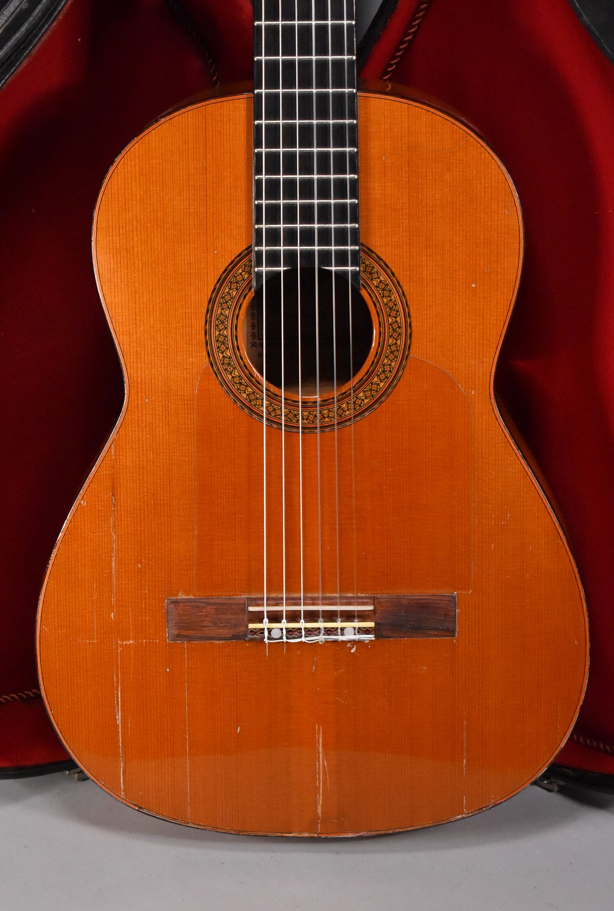 The classical guitar's natural finish body shows heavy play wear and checking, with a clear pickguard and ornate rosette.