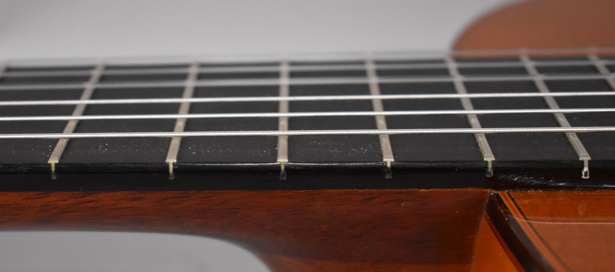 Close-up of the classical guitar's dark fretboard and light nylon strings, showing some dust and wear on the frets.