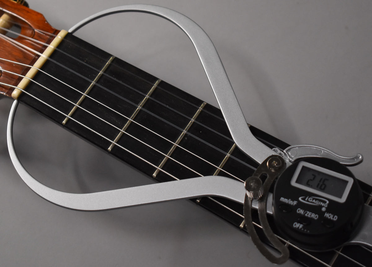 Close-up of the guitar's dark fretboard and light-colored nut, with a silver digital caliper measuring the string height at 2.16.