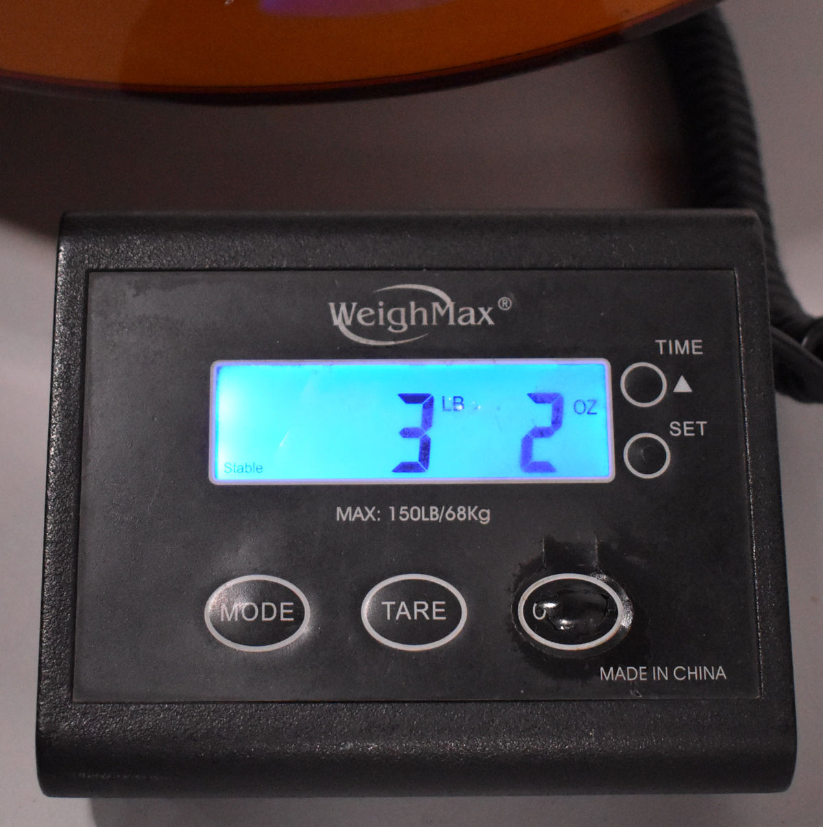 A close-up of a digital scale displaying "3 LB 2 OZ" in blue light, with "WeighMax" and "MADE IN CHINA" visible.