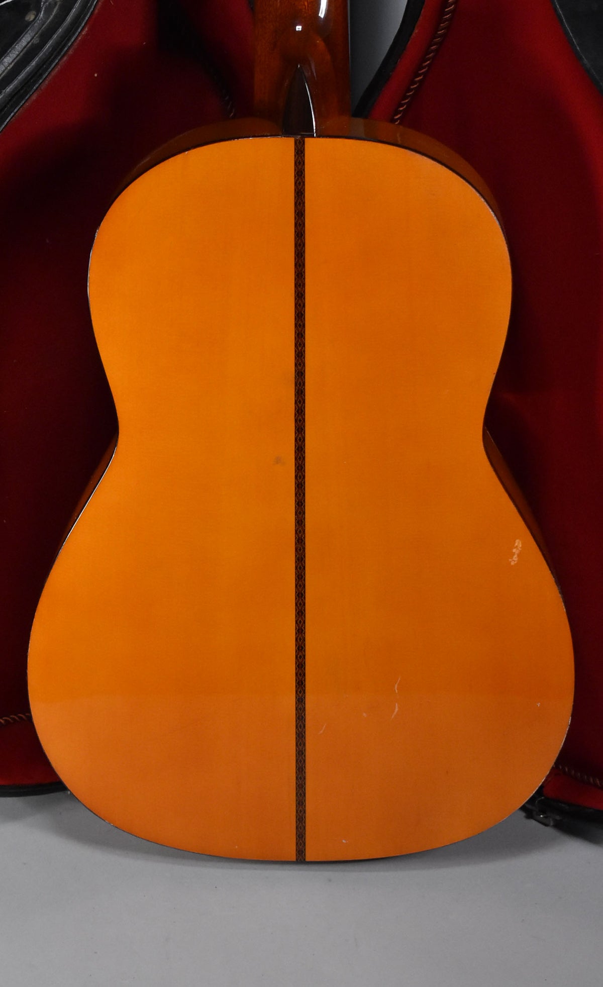 The back of the classical guitar, with a natural finish, shows a dark decorative center strip and light surface scratches.