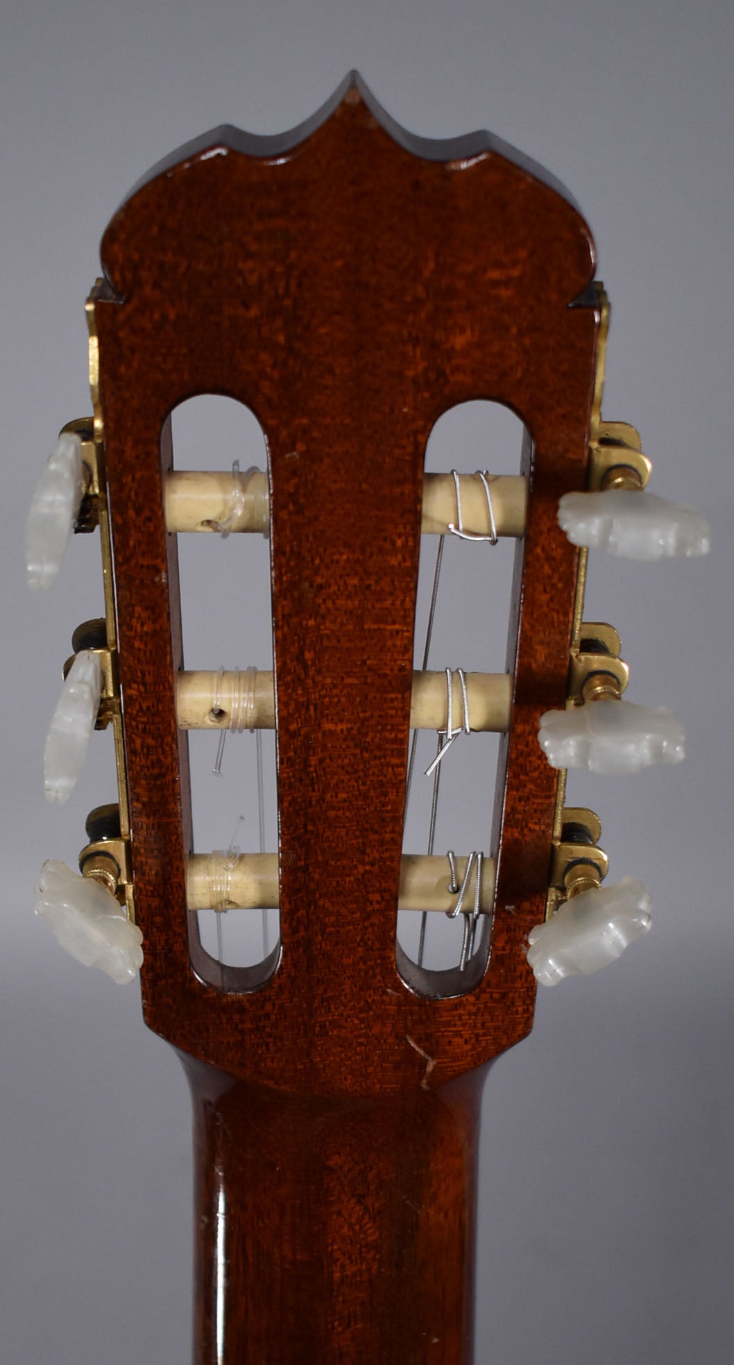 Rear view of the classical guitar's dark brown headstock and neck, showing six white tuning pegs and light wear on the finish.
