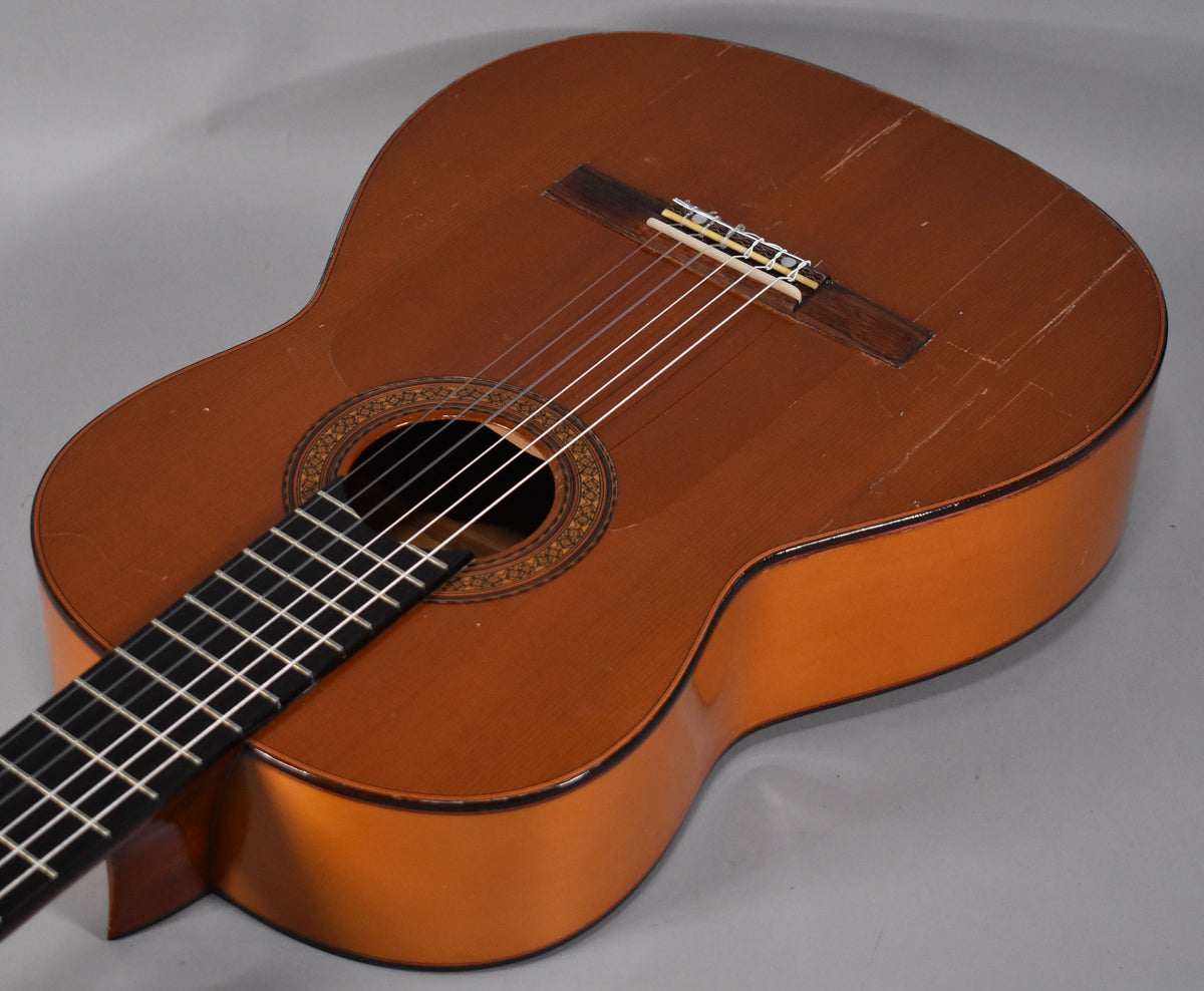 Angled view of a natural finish classical guitar, showing the body, bridge, soundhole, and lower fretboard with visible finish checking.