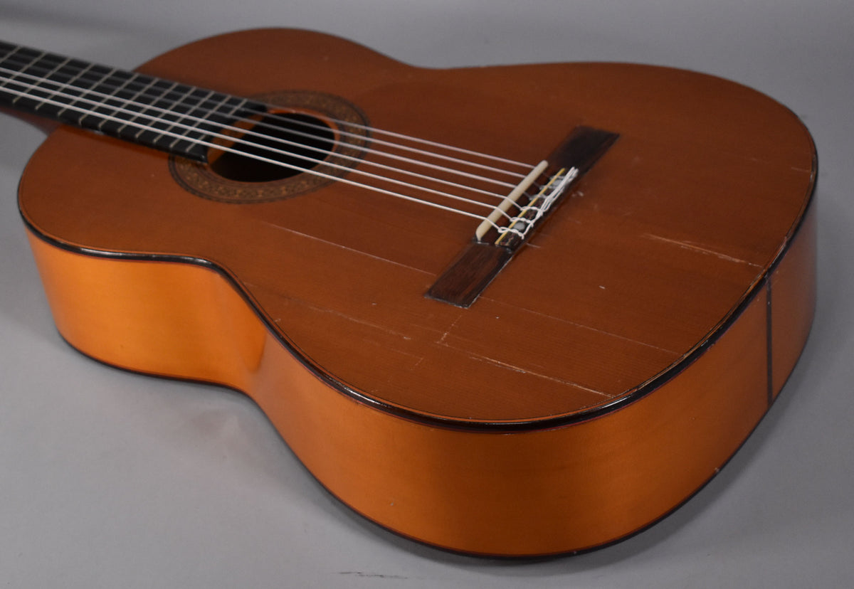 Close-up of the classical guitar's body, showing the natural finish top with many scratches and a dark wood bridge.