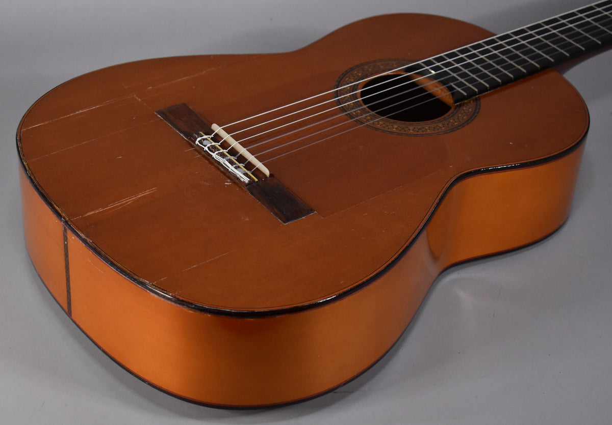 The classical guitar's natural finish body and sides are visible from the lower bout, showing many scratches and finish checking.