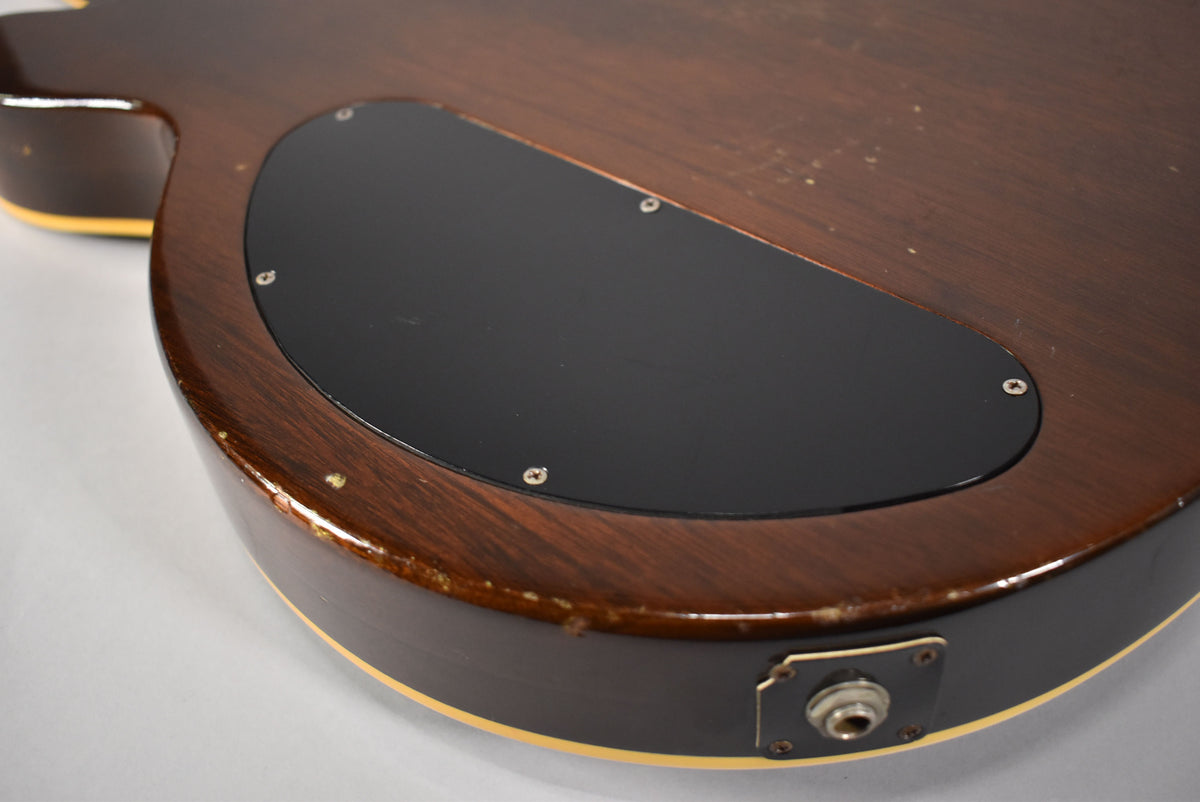 The dark walnut guitar body, with a black control cavity cover, shows significant wear and checking around the output jack.