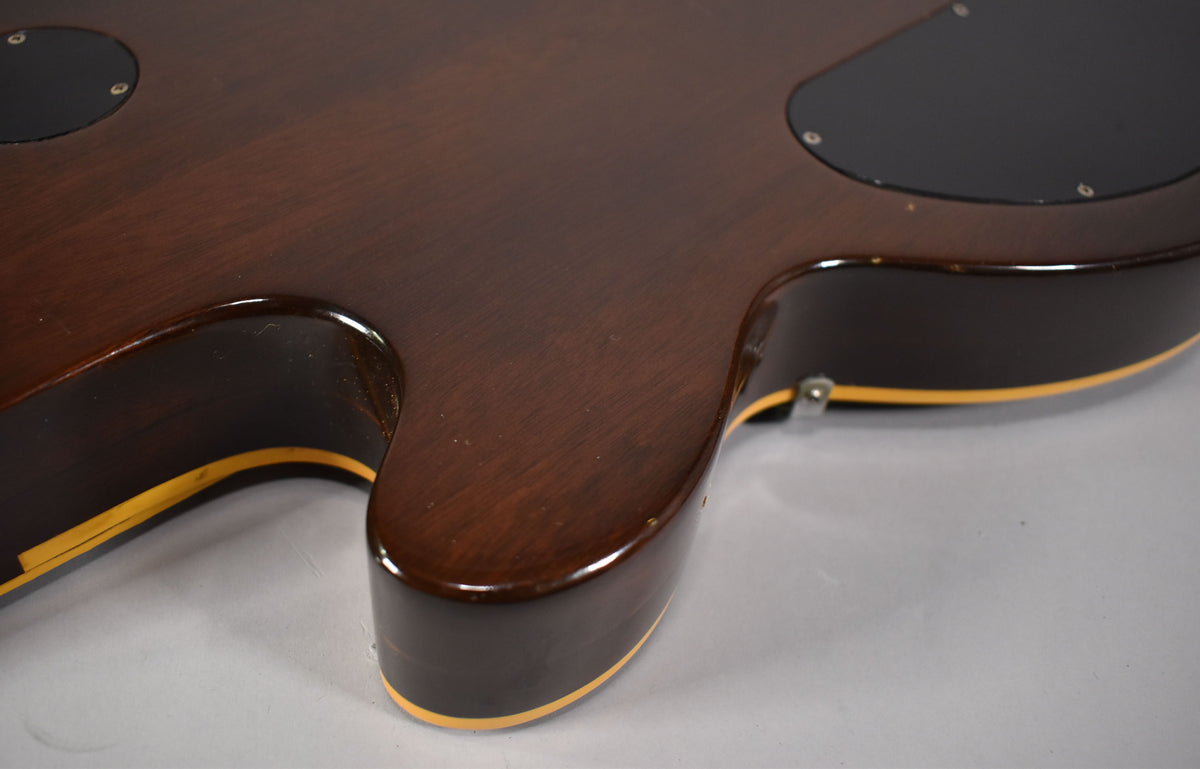 The guitar's dark walnut back, with cream binding and a glossy finish, shows light wear and two black control cavity covers.