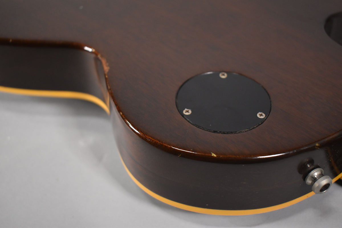 Close-up of the guitar's dark walnut body, showing a black control cavity cover, output jack, and binding with some chips and wear.