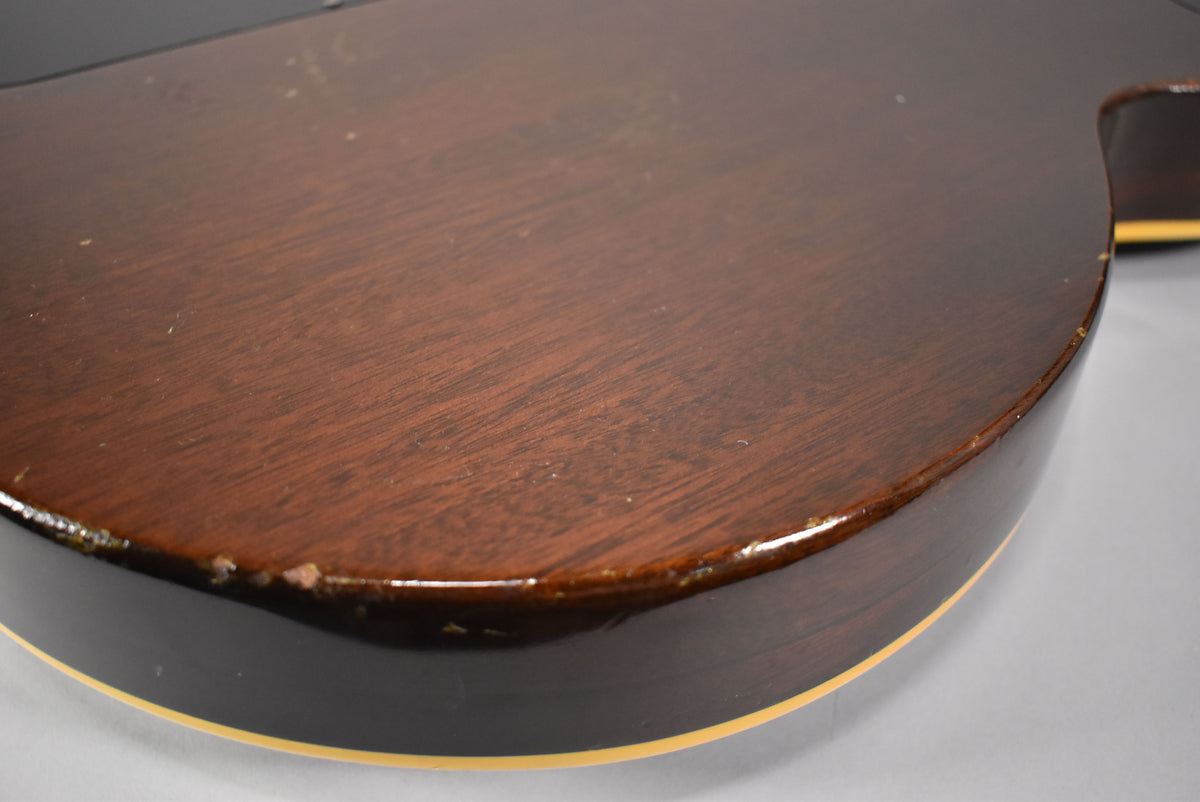 Close-up of the guitar's lower bout, showing a dark walnut finish with visible wood grain, nicks, and wear along the binding.