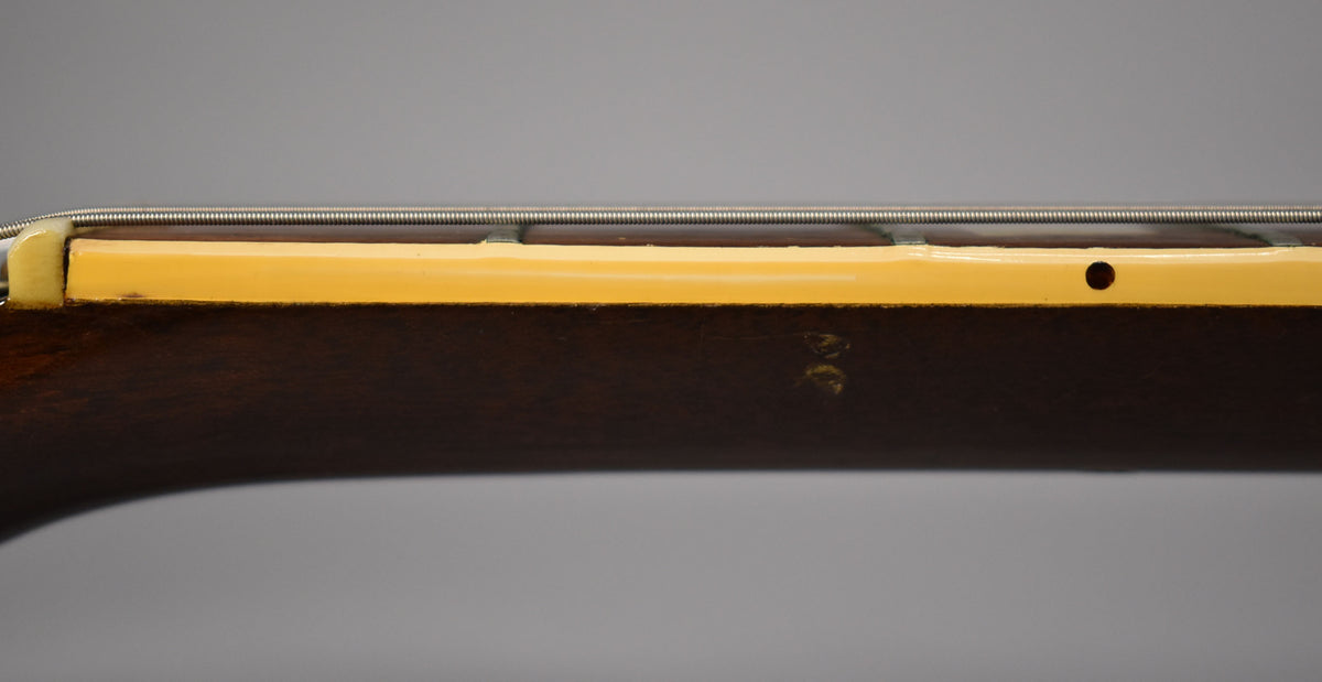 The guitar's dark walnut neck, viewed from the side, shows a cream binding with a small black dot and some wear on the finish.