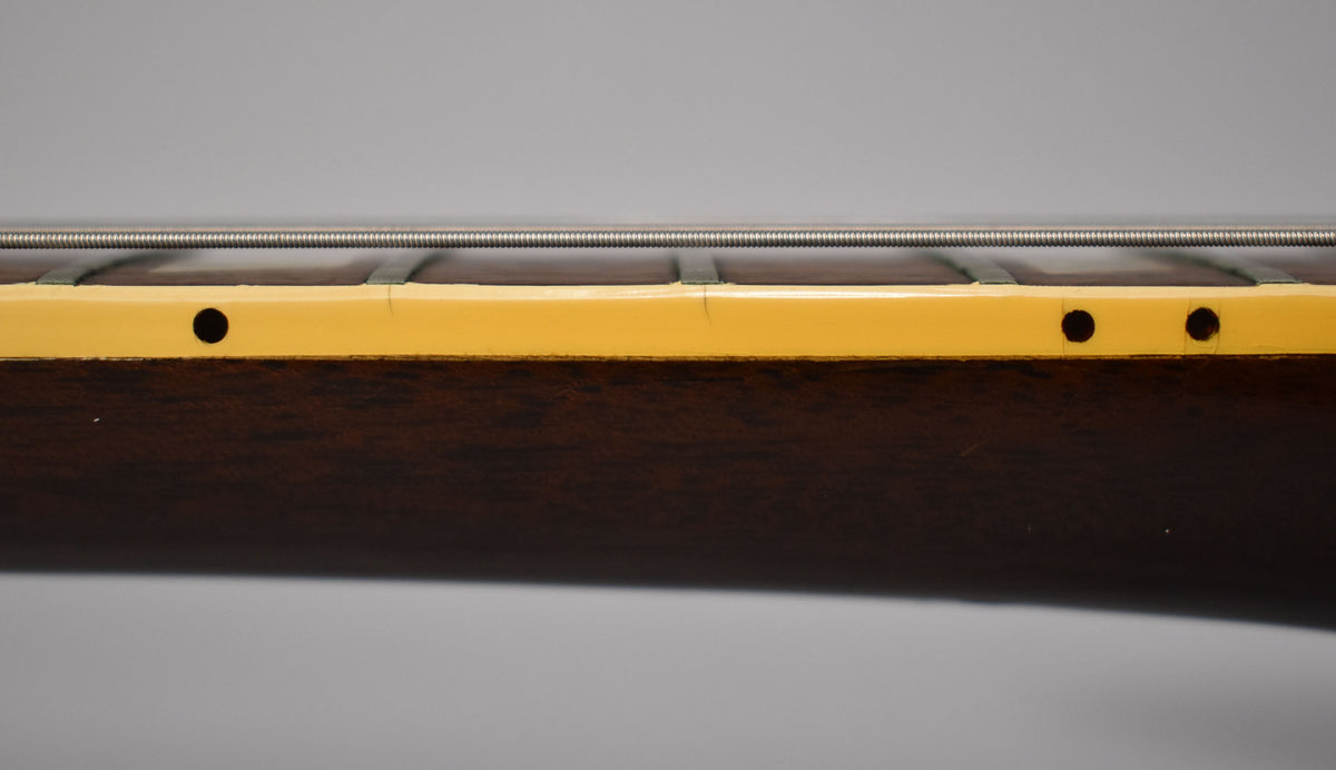 Close-up of the dark walnut neck, showing the cream binding with side dots and fine cracks, and a single wound string.